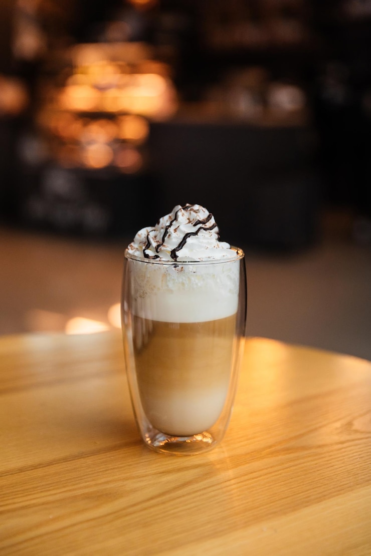 Foto latte cappuccino con schiuma e panna in una tazza trasparente su un tavolo in un bar caffè con dessert a piacere immagine isolata di dessert su sfondo bokeh