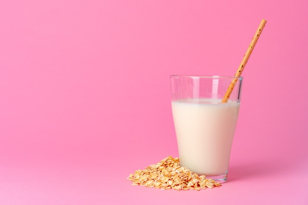 Latte d'avena in cristalleria e fiocchi d'avena secchi su sfondo rosa