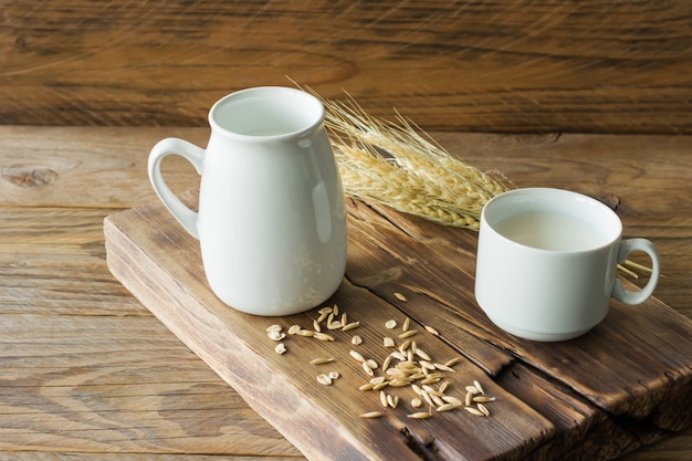 Latte d'avena in una brocca di vetro e farina d'avena in una tazza su un tavolo di legno.