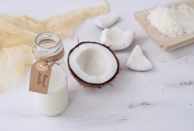 Latte di cocco fresco in bottiglia di vetro con la metà della noce di cocco fresca su rustico bianco in legno