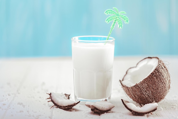 Latte di cocco in vetro con frutta di cocco su tavola di legno Concetto di latte alternativo Bevanda tropicale