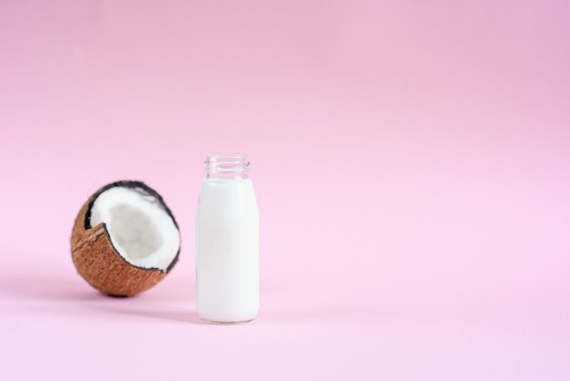 Latte di cocco nella bottiglia di vetro e noce di cocco fresca su fondo rosa.