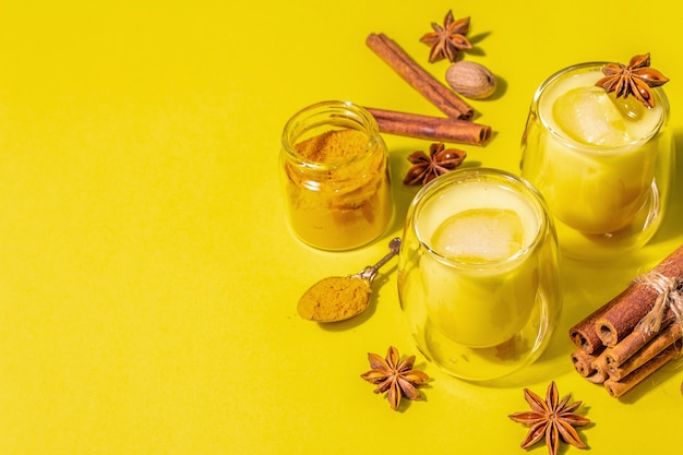 Latte di curcuma dorata con ghiaccio. Cannella, noce moscata, spezie anice. Concetto di bevanda salutare alla moda. Una moderna luce dura, ombra scura, sfondo giallo brillante, spazio di copia