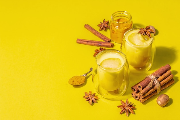 Latte di curcuma dorata con ghiaccio. Cannella, noce moscata, spezie anice. Concetto di bevanda salutare alla moda. Una moderna luce dura, ombra scura, sfondo giallo brillante, vista dall'alto