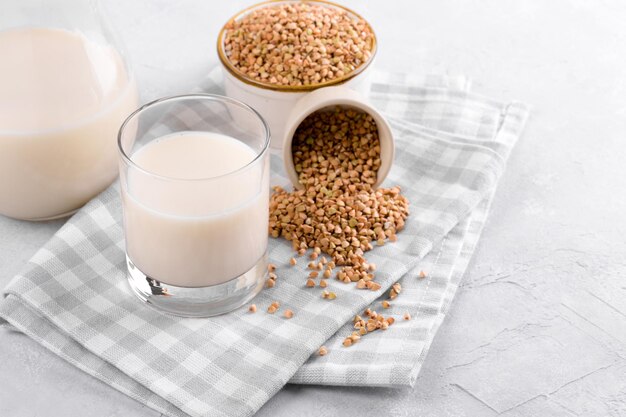 Latte di grano saraceno vegano non diario in vetro con semole di grano saraceno in una ciotola e su tavola di pietra bianca da vicino