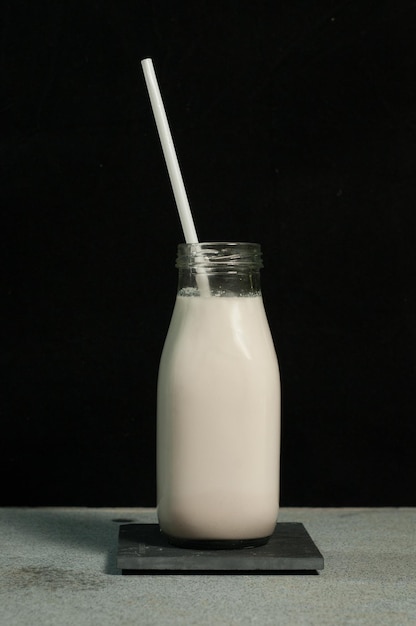 Latte di mandorle in bicchiere con paglia su tavola su sfondo nero