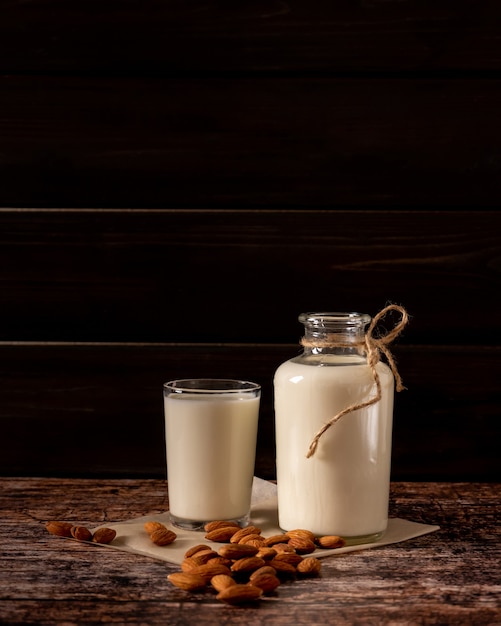 Latte di mandorle in una bottiglia e un bicchiere, su fondo di legno vintage scuro, con copia-spazio