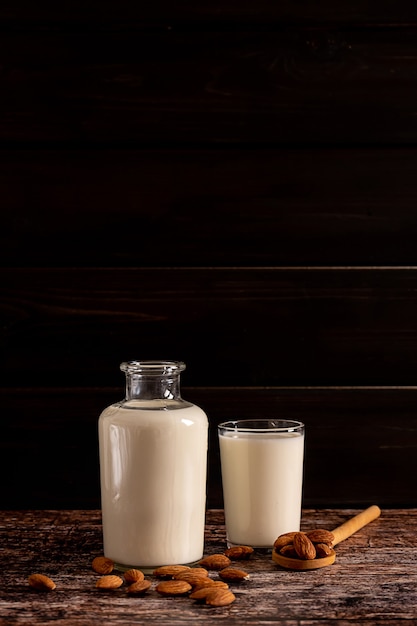 Latte di mandorle in una bottiglia e un bicchiere, su fondo di legno vintage scuro, con copia-spazio