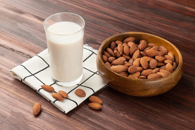 Latte di mandorle nel bicchiere con mandorle in ciotola di legno sul tavolo, spuntino sano, cibo vegetariano.