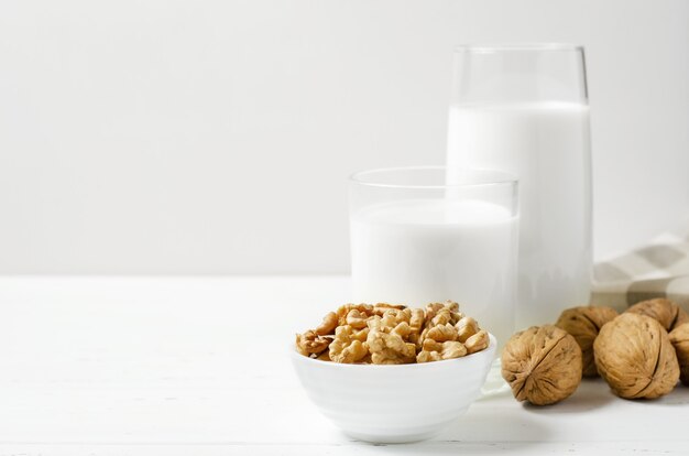 Latte di noci e noci su un fondo di legno bianco. Prodotti contenenti proteine vegetali, vitamine e aminoacidi utili. Copia spazio.