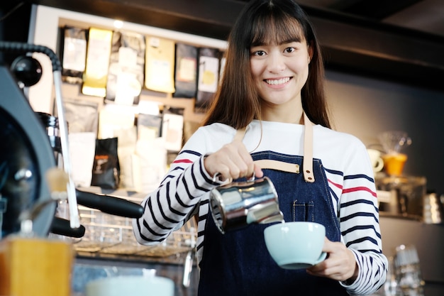 Latte di versamento di giovane barista asiatico delle donne sulla tazza di caffè.