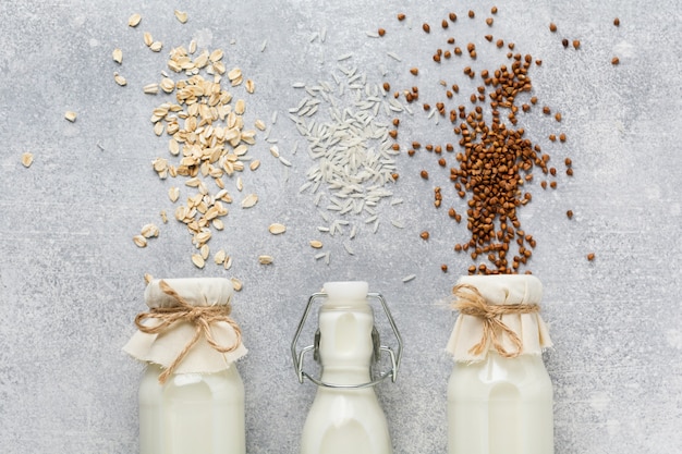 Latte dietetico vegetariano di riso ai cereali, grano saraceno e avena, tre tipi di fatti in casa su una tendenza del cemento grigio.