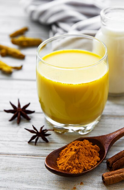 Latte dorato con cannella, curcuma, zenzero e miele su una superficie di legno bianca