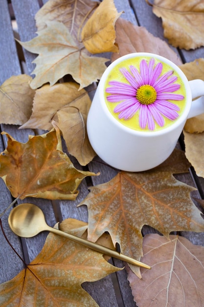 Latte dorato in una tazza bianca decorata con una margherita rosa