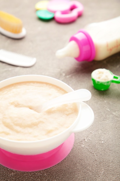 Latte e ciotola con porridge per bambino su grigio