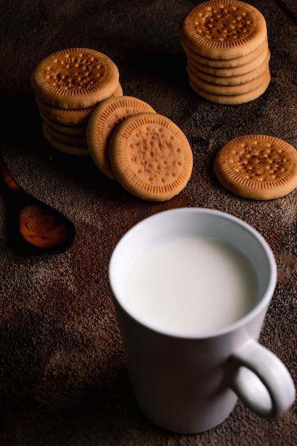 Latte fresco con i biscotti fatti in casa su un tavolo di legno, sfondo scuro.