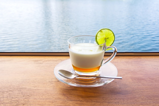 Latte fresco del yogurt del limone in un vetro libero disposto su una tavola di legno marrone con la superficie dell&#39;acqua di mare.