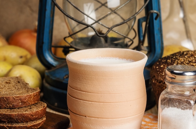 latte in ceramica pane di segale saliera verdure e lanterna di cherosene su un tavolo di legno