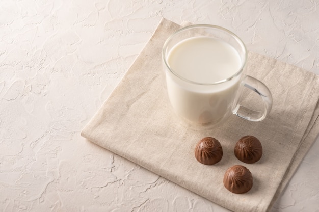 Latte in una tazza e cioccolatini su un tovagliolo di lino su sfondo chiaro.