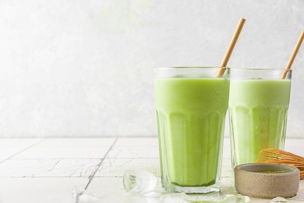 Latte matcha verde ghiacciato in bicchieri con una cannuccia su sfondo bianco Bevanda estiva fredda Bevanda disintossicante salutare