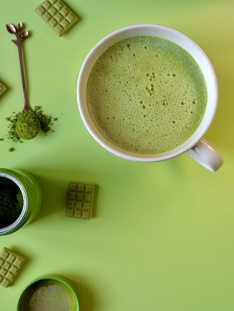 Latte matcha verde in una tazza bianca e barrette di cioccolato con tè matcha su sfondo verde, vista dall'alto