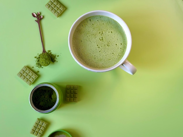 Latte matcha verde in una tazza bianca e barrette di cioccolato con tè matcha su sfondo verde