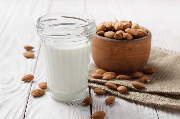 Latte o yogurt in barattolo di vetro su tavola di legno bianca con ciotola di mandorle su tovagliolo di canapa da parte