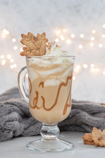 Latte speziato di zucca in una tazza di vetro con caramello e cannella con decorazione autunnale