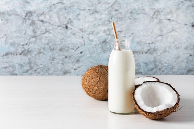 Latte vegano al cocco in bottiglia con metà di cocco su tavola di legno Latte vegano alternativo alle noci