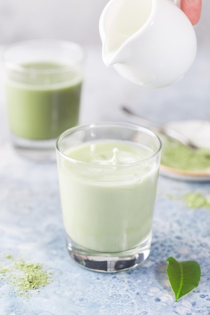 Latte verde Matcha ghiacciato in bicchieri con polvere di matcha su sfondo chiaro.