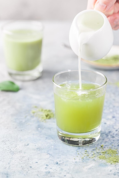 Latte verde Matcha ghiacciato in bicchieri con polvere di matcha su sfondo chiaro.