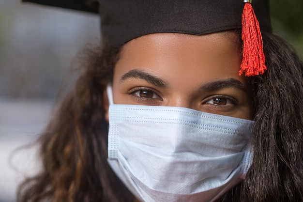 Laureato. Una ragazza carina dalla pelle scura con un berretto accademico e una maschera preventiva