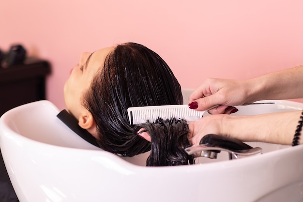 Lavaggio con shampoo della testa femminile con lunghi capelli castani nel salone di parrucchiere