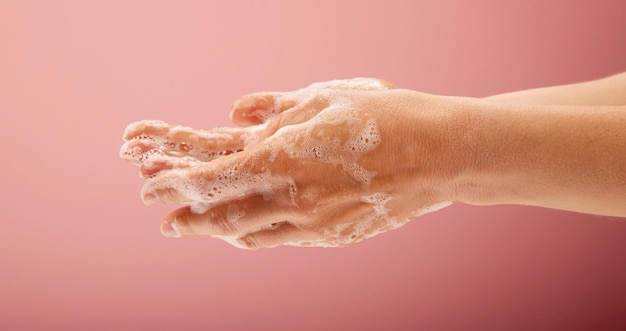 Lavaggio delle mani della donna con schiuma di sapone e acqua su sfondo rosa brillante