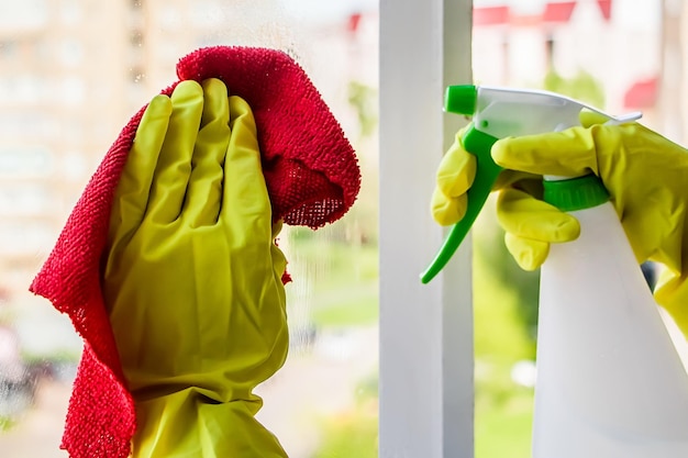 Lavaggio vetri e pulizia della casa. La governante in guanti gialli lava e pulisce il vetro sporco.