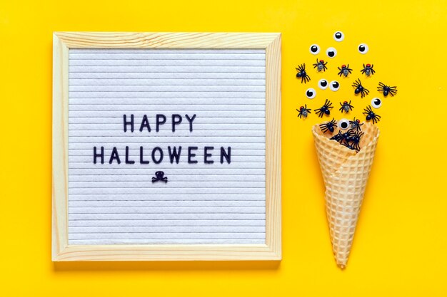 Lavagna in feltro con testo, citazione, ragni neri e mosche, occhi finti che strisciano fuori dal cono gelato. Vista dall'alto piatto lay Happy Halloween concetto creativo Holiday card.