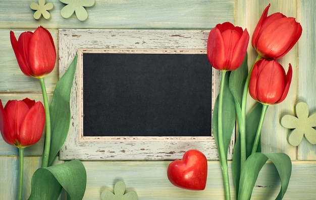Lavagna incorniciata con tulipani rossi su legno verde, spazio per il testo