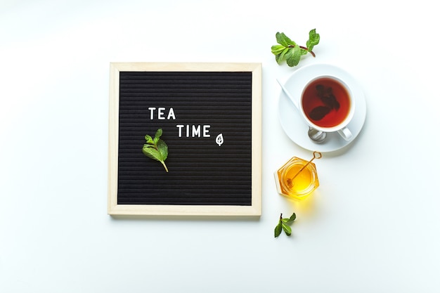 Lavagna nera per l'ora del tè con testo su tavolo di marmo con tazza di tè in vetro con foglie di menta