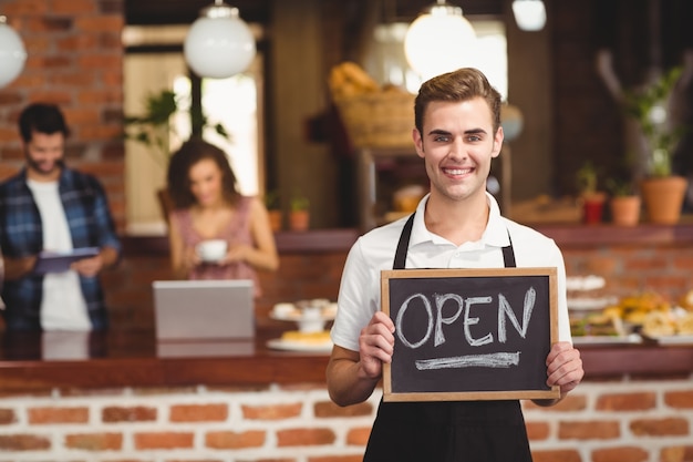 Lavagna sorridente della tenuta di barista con il segno aperto