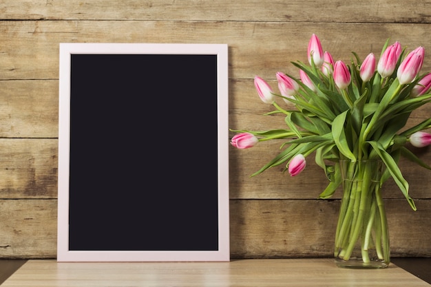 Lavagna trasparente, vaso con tulipani su superficie di legno. Il concetto dell'inizio della primavera, le vacanze. Copia spazio.