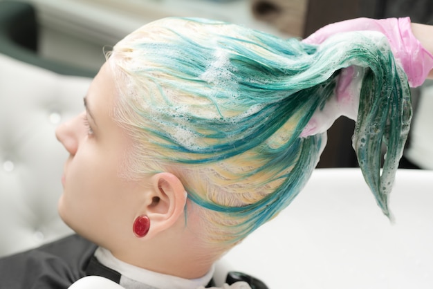 Lavare il colore dei capelli color smeraldo della giovane donna con shampoo nel salone di bellezza beauty