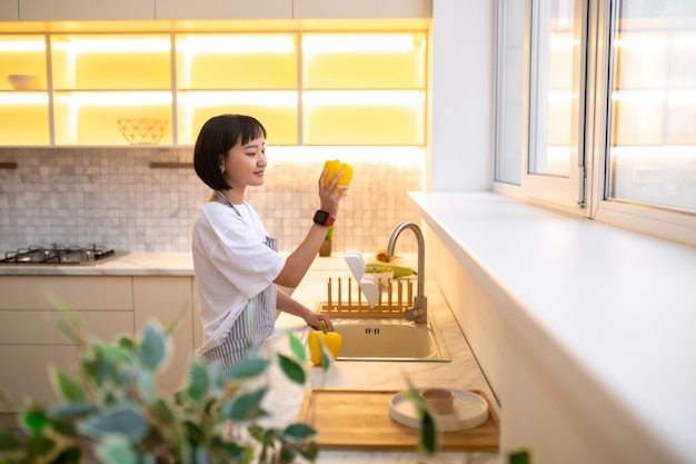 Lavare le verdure. Giovane donna sveglia nel grembiule che lava le verdure in cucina