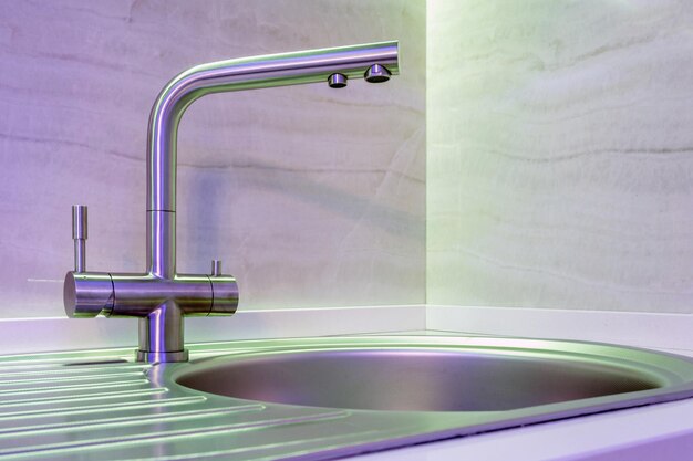 Lavello del rubinetto dell'acqua con rubinetto nella costosa cucina a soppalco con luce al neon
