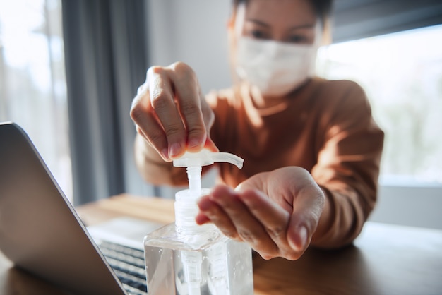 Lavorando da casa, protezione da virus Corona, Primo piano che si pulisce le mani con gel disinfettante, Donna in quarantena per coronavirus con maschera protettiva.