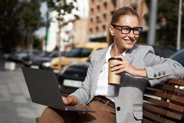 Lavorando da ogni parte ritratto di una bella donna d'affari felice che beve caffè e usa