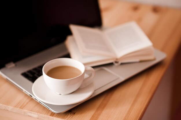 Lavorare a casa come concetto di libero professionista. Tazza di caffè con libro aperto e laptop in camera. Buon giorno.