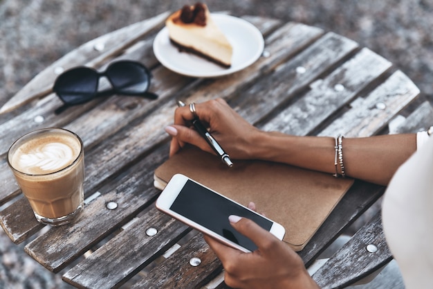 Lavorare all'aperto. Primo piano di una giovane donna che usa il suo smartphone mentre è seduta al ristorante all'aperto