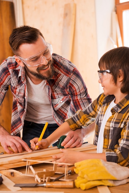 Lavorare insieme. Sorridente giovane carpentiere maschio e suo figlio che si guardano mentre lavorano in officina