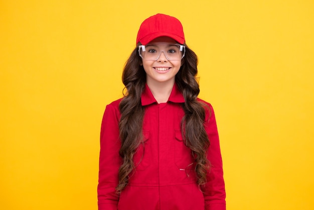 Lavoratore adolescente bambino che indossa tute berretto rosso e proteggere gli occhiali Studio girato ritratto isolato su sfondo giallo faccia felice emozioni positive e sorridenti della ragazza adolescente