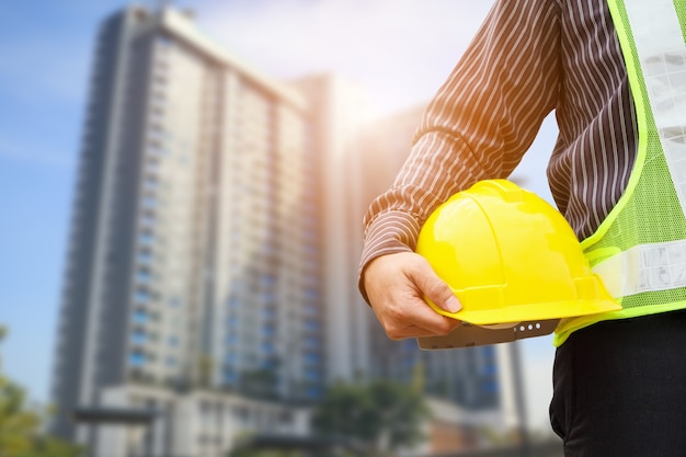 Lavoratore asiatico dell'ingegnere o dell'architetto della costruzione dell'uomo di affari con il casco protettivo giallo al grande cantiere del condominio